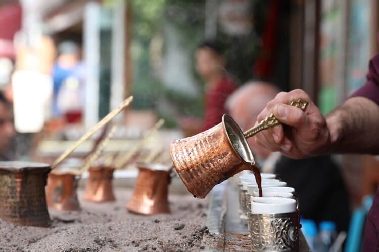 A hand pouring Turkish coffee into white cups from sand.