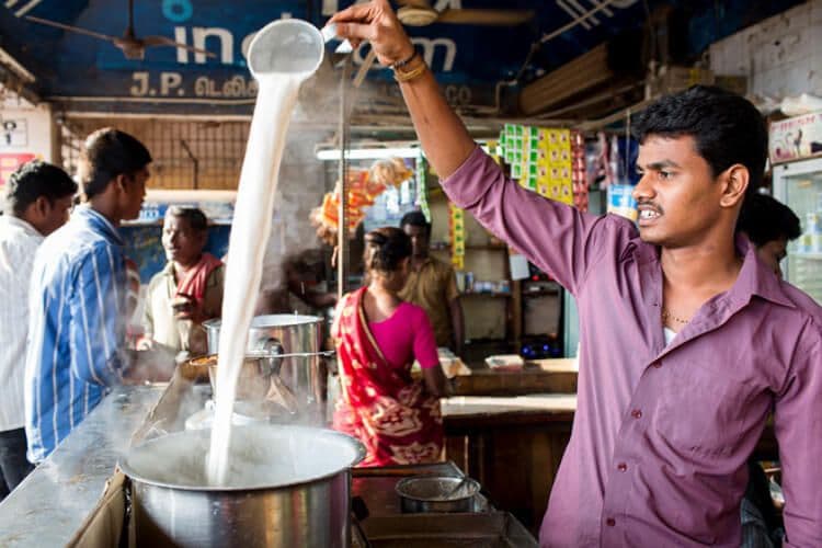 A man pouring milky coffee from high in India.